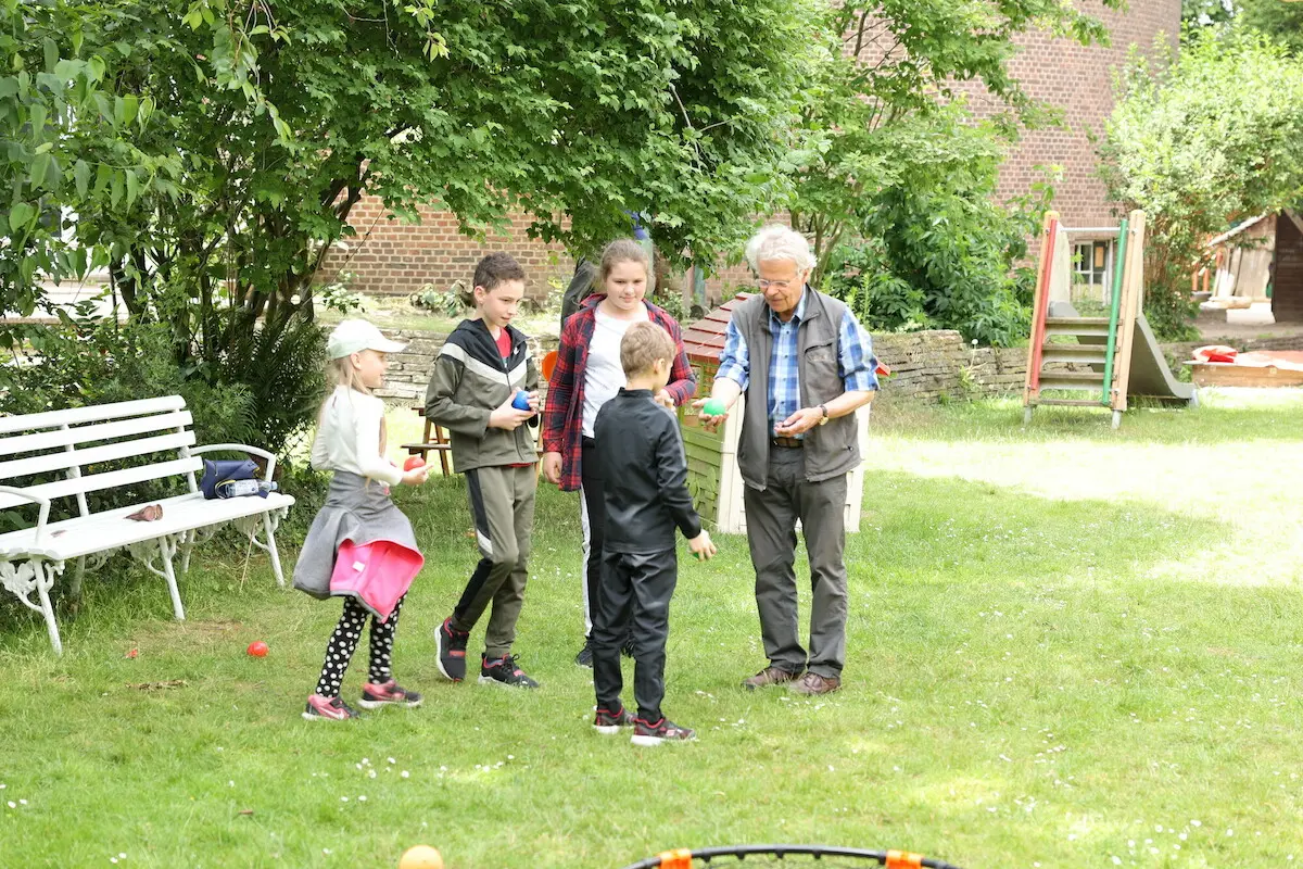 Kinder und Erwachsene spielen, sprechen, essen miteinander, draußen im Gemeindegarten